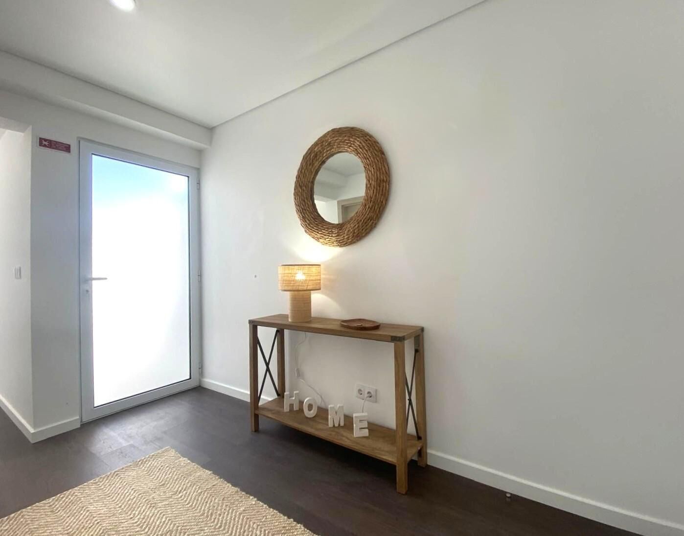 A hallway with a wooden console table, a wall-mounted mirror, and a lit floor lamp.