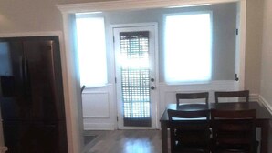 Ein offener Wohnbereich mit Esstisch und Stühlen, eine Küche inklusive Kühlschrank sowie eine Tür, die auf einen Balkon führt.