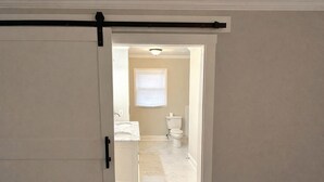Ein Flur, der zu einem Badezimmer mit Toilette, Waschbecken und Fenster führt.