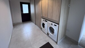 A laundry room with two front-loading washing machines, a ceiling light fixture, and a door leading to another room. - Large Modern Cottage, near the Medieval town of Athenry, Co Galway (North Athenry)