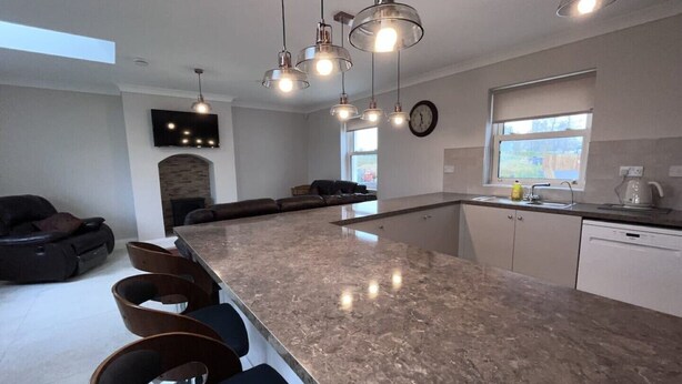 A modern kitchen with a large island, bar stools, pendant lighting, and a stone fireplace. - Large Modern Cottage, near the Medieval town of Athenry, Co Galway (North Athenry)