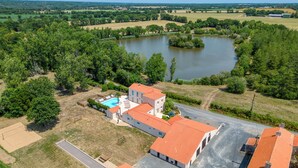 A large building with a swimming pool, surrounded by greenery and a lake.