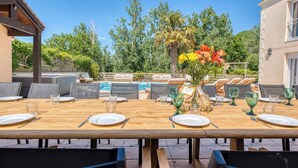 An outdoor dining area with a pool, lounge chairs, and a wooden table set for a meal.