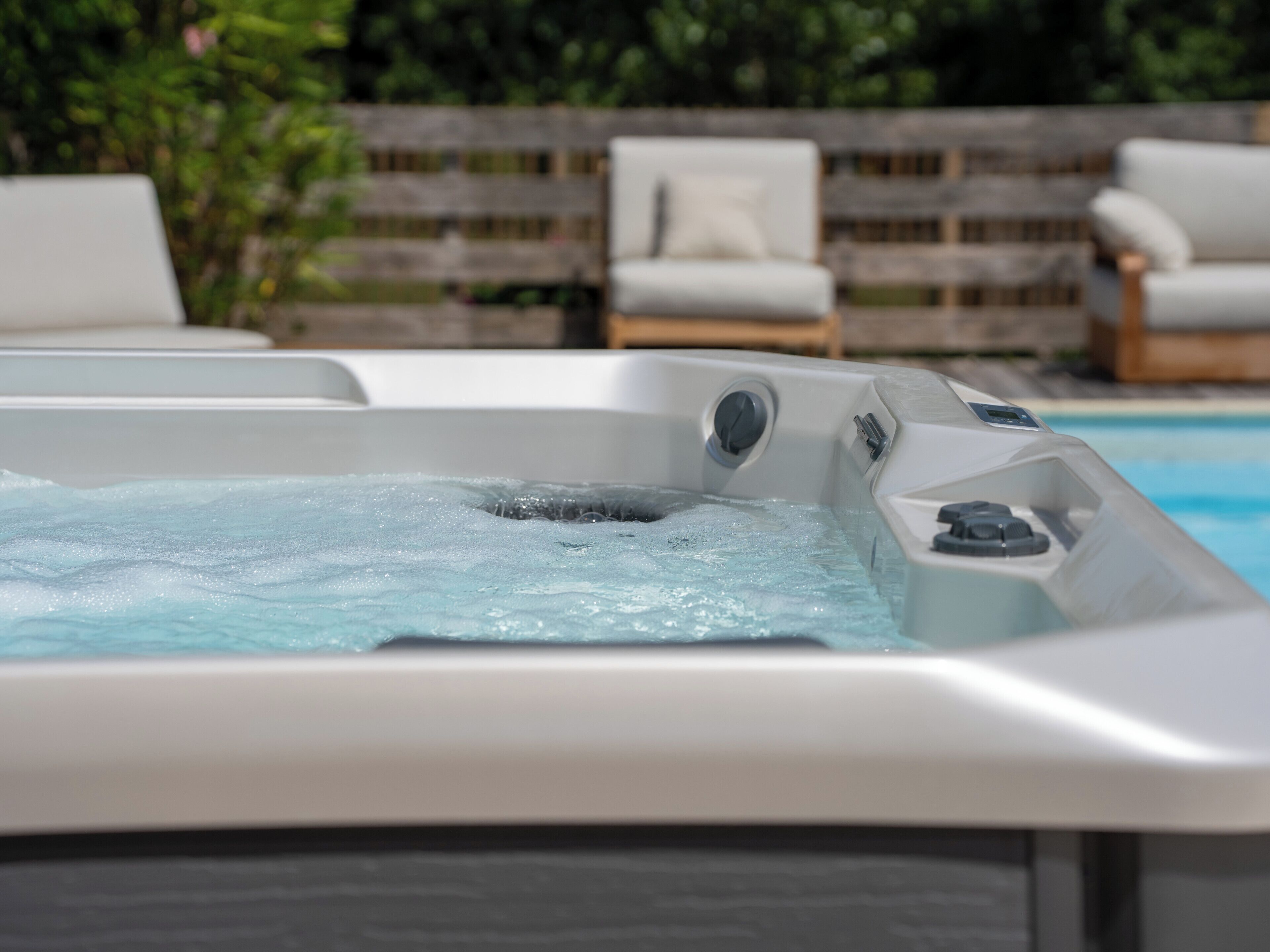 Ein Whirlpool mit Bedienfeld, umgeben von Liegestühlen und einem Holzzaun.