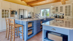A kitchen with white cabinets, a blue island, wooden chairs, and a wooden ceiling.