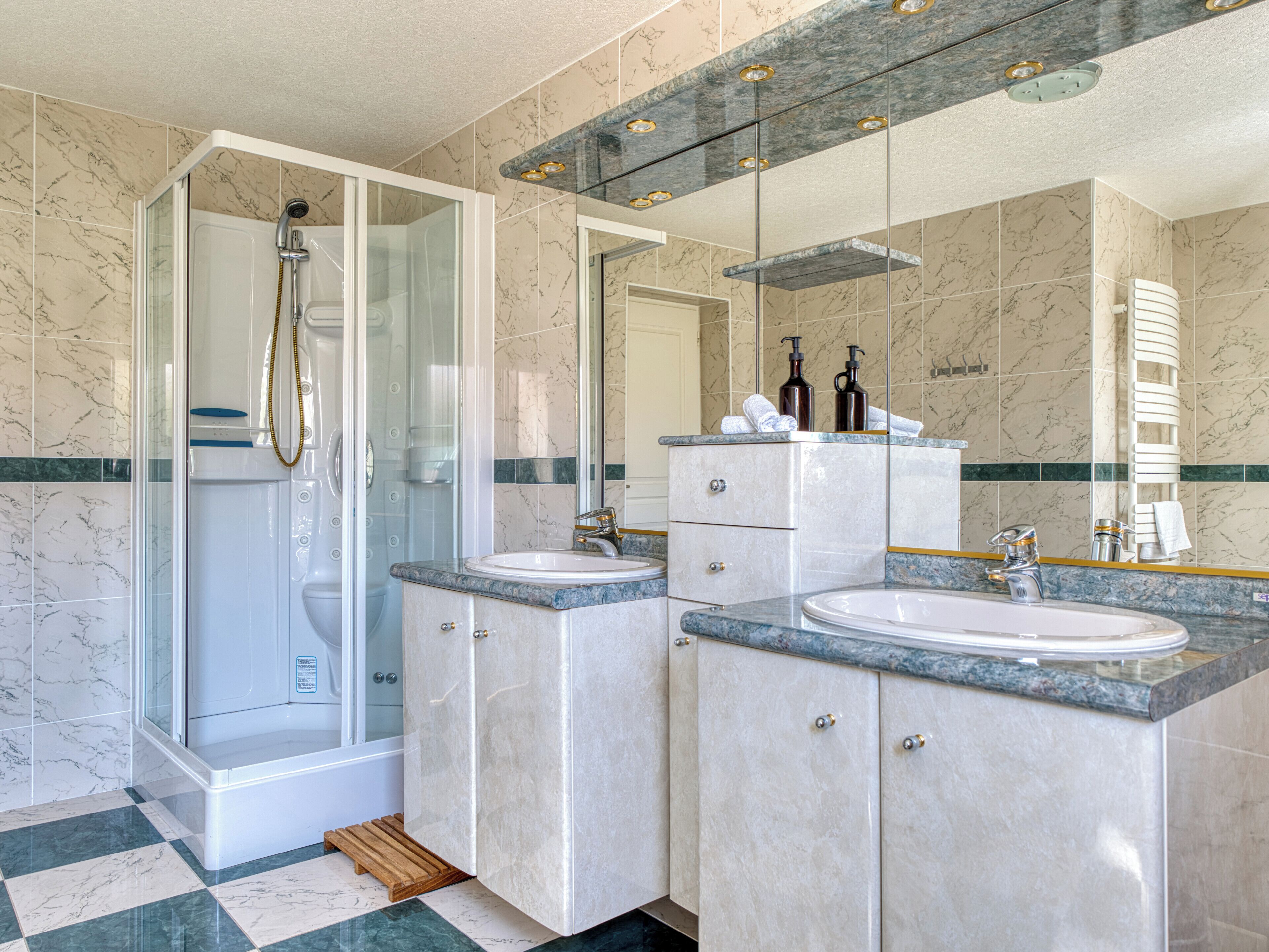 Une salle de bain moderne dotée d’une douche à parois de verre, de deux lavabos et de plans de travail en marbre.