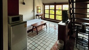 Une pièce avec un sol carrelé, un lit, une table, un banc, un réfrigérateur, une fenêtre et une échelle.