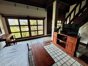 Ein Zimmer mit großem Fenster, einem Holztisch, einem Fernseher und einem Fliesenboden.