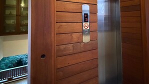 Une porte d’ascenseur en bois, dotée d’un écran numérique et d’un panneau indiquant qu’il est interdit de fumer.