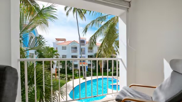 Ein Balkon mit Blick auf einen Pool, zwei Stühle und einem weißen Geländer.