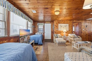 Ein Zimmer mit Holzwänden und -decken, einem Bett, einem Sofa, einem Sessel, einer Lampe und einem Bild an der Wand.