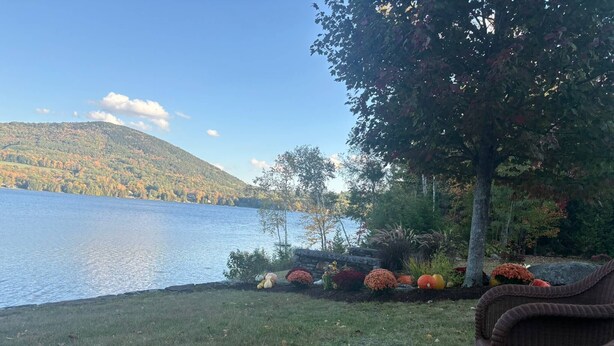 A lakeside view with wicker furniture, a stone wall, and autumn foliage.