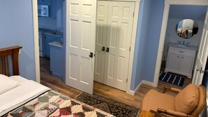 A bedroom with a bed, a chair, a closet, and a bathroom visible through an open door.