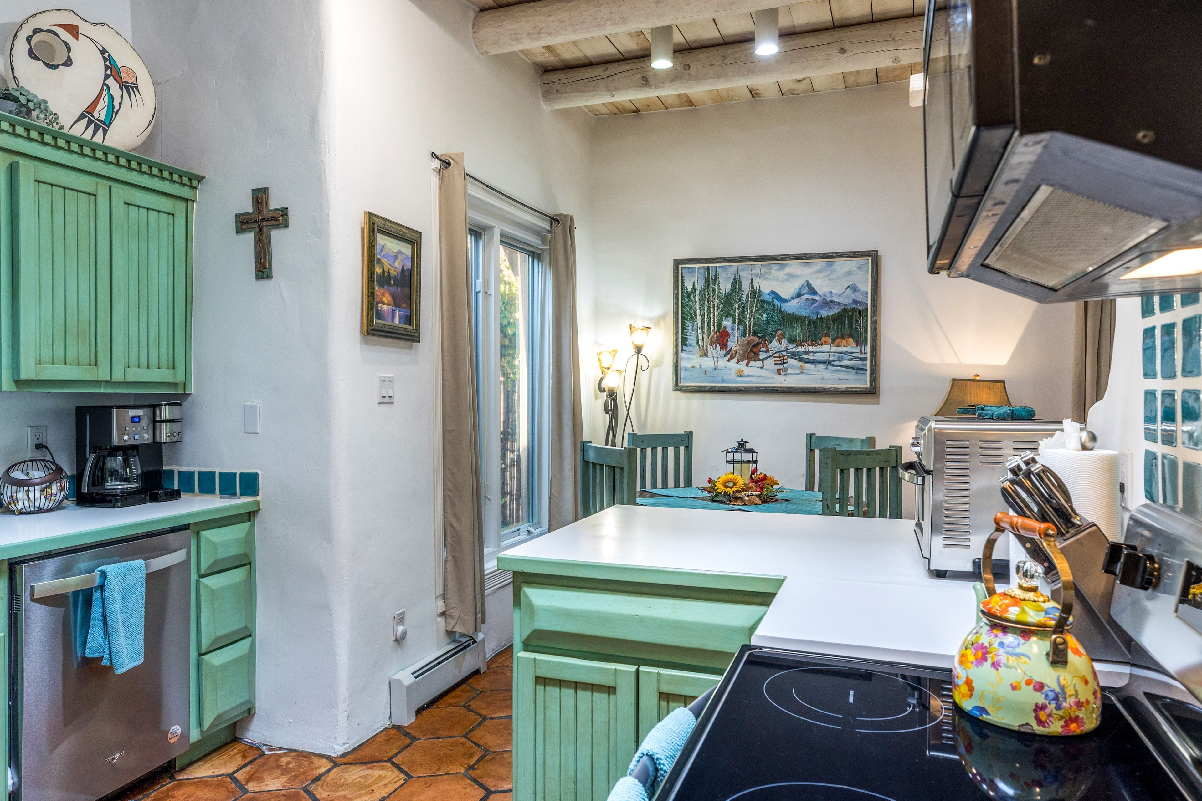 Une cuisine avec des meubles de couleur verte, une cuisinière, une machine à café et un tableau accroché au mur.