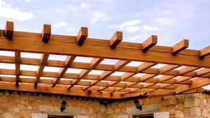 An outdoor patio with wicker furniture, a stone wall, and a wooden pergola.