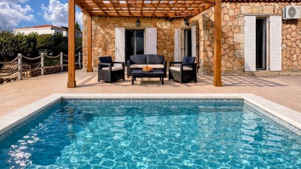 A poolside area with a pergola, stone building, and a clear blue sky.