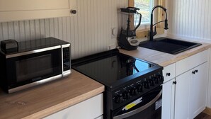 A compact kitchen with a microwave, stove, sink, and a blender on the countertop. - Tiny House in the Woods (Oakland)