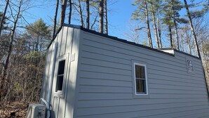 A small, single-story cabin with a sloped roof, surrounded by tall pine trees. - Tiny House in the Woods (Oakland)