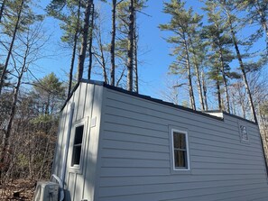 A small, single-story cabin with a sloped roof, surrounded by tall pine trees. - Tiny House in the Woods (Oakland)