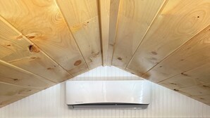 A room with a sloped ceiling, wooden beams, a black mattress, and a white wall with a window. - Tiny House in the Woods (Oakland)