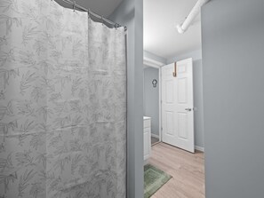 Ein Badezimmer mit einer weißen Tür, einem Duschvorhang mit Blättermotiv und einem grünen Teppich.