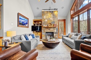 A spacious living room with a stone fireplace, two sofas, a coffee table, and a television. - Mountain Village Retreat - Hot Tub + Ski-In/Out (Mountain Village)