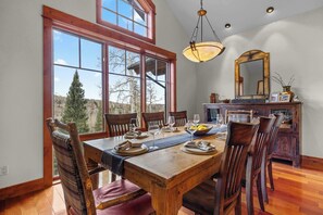A dining room with a wooden table set for six, large windows, and a mirror on the wall. - Mountain Village Retreat - Hot Tub + Ski-In/Out (Mountain Village)