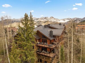 A multi-story log cabin with a balcony, surrounded by trees and mountains. - Mountain Village Retreat - Hot Tub + Ski-In/Out (Mountain Village)