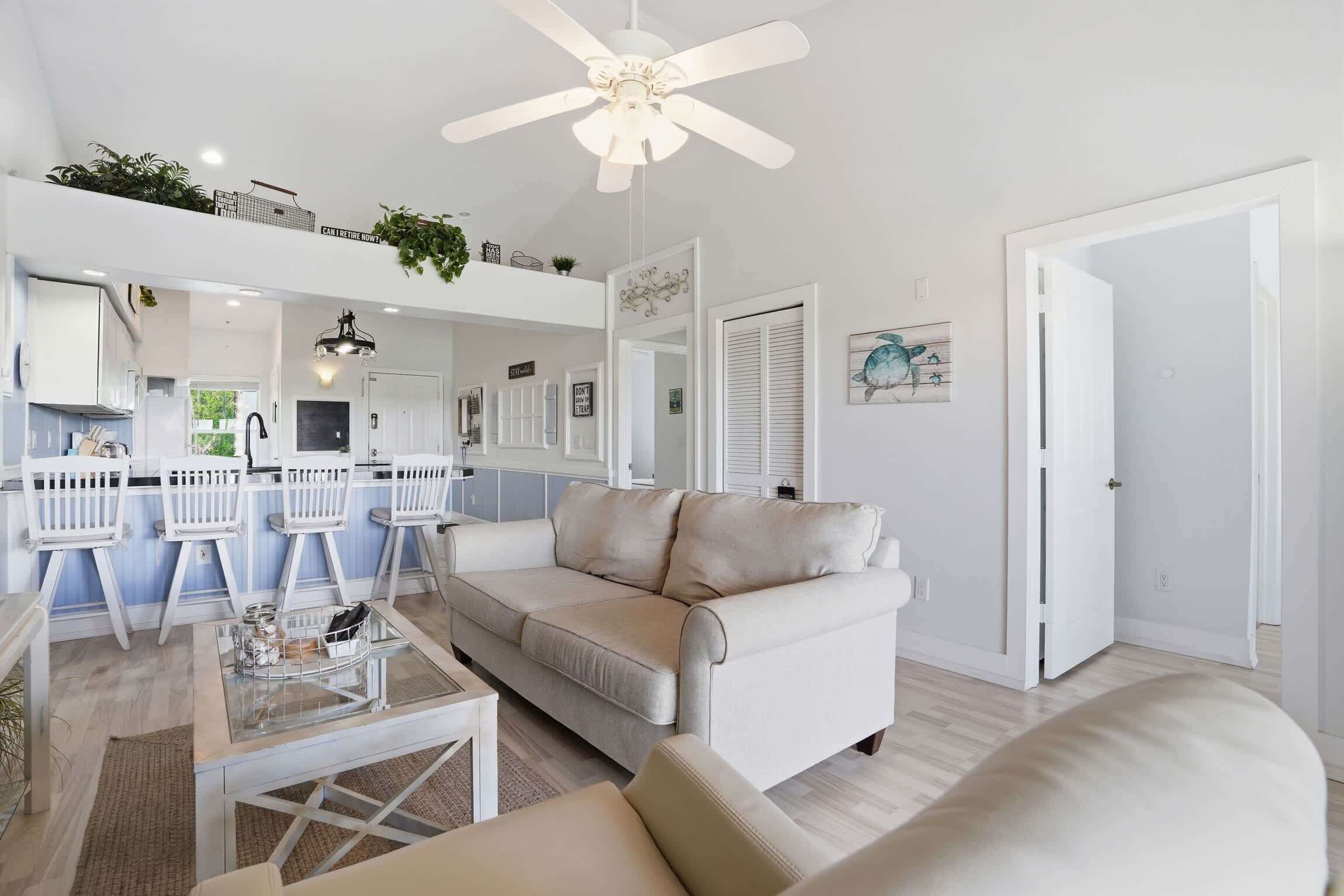 A spacious living area with a white sofa, a glass coffee table, and a ceiling fan.