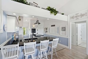 A modern kitchen with a central island, white chairs, and a chandelier. - #123 - Lake View, Tall Ceilings W Rare Floor Plan (Naples)