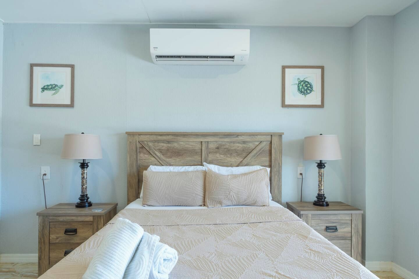 A bedroom with a wooden headboard, two bedside tables with lamps, a bed with a patterned bedspread, and two framed pictures on the wall.