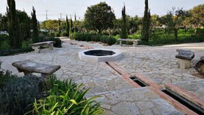 Um jardim com piso de pedra, bancos e uma lareira central.