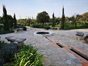 A stone-paved garden with benches and a central fire pit. - Quinta Nova – Charming Guest House – Arrábida (Azeitão)