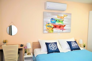 A hotel room with a bed, a desk, a chair, a mirror, and a wall-mounted air conditioner. - Casa Luigi Studio 2 – Unique View and Prime Location (Rovinj)