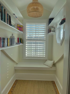 A room with a built-in bench, a large window with blinds, and shelves with books and decorative items. - Spacious 6-bedroom house in charming Deltaville, VA (Deltaville)