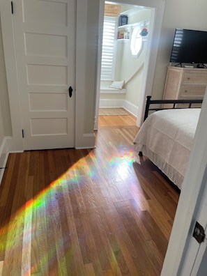 A room with a wooden floor, a bed, a television, and a door leading to another room. - Spacious 6-bedroom house in charming Deltaville, VA (Deltaville)