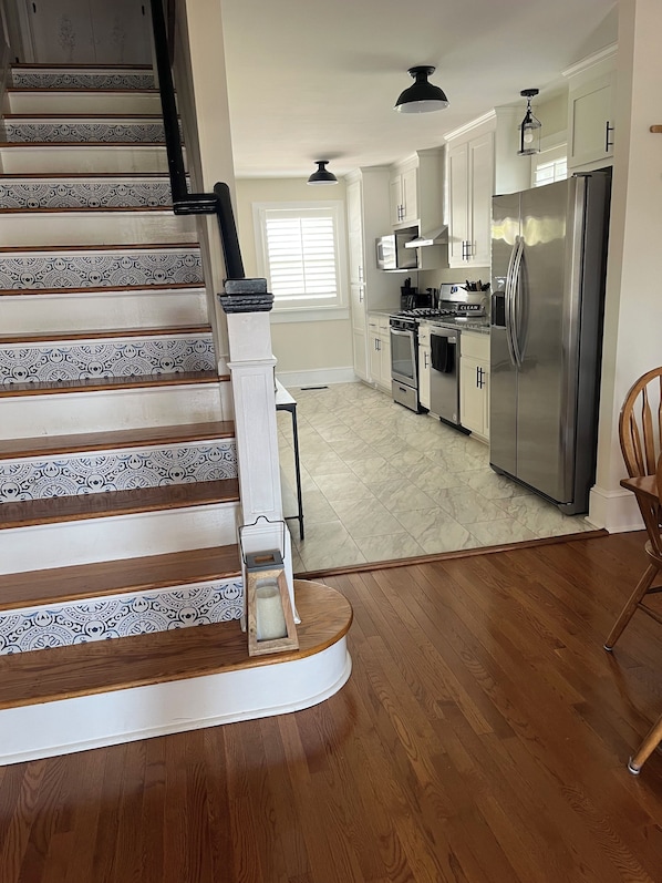 A kitchen with a stainless steel refrigerator, a stove, and a microwave. There is a wooden staircase with patterned railings leading to another level. - Spacious 6-bedroom house in charming Deltaville, VA (Deltaville)