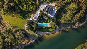 Vista aérea de una casa con piscina, rodeada de árboles y una masa de agua.