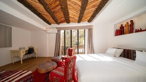 A bedroom with a large bed, a wooden ceiling, a desk, a chair, and a window with curtains. - The House of Designers by BCKART GALLERY (Lalla Takarkoust)