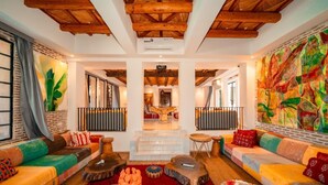 A spacious living area with a high ceiling, wooden beams, colorful sofas, and a large abstract painting. - The House of Designers by BCKART GALLERY (Lalla Takarkoust)