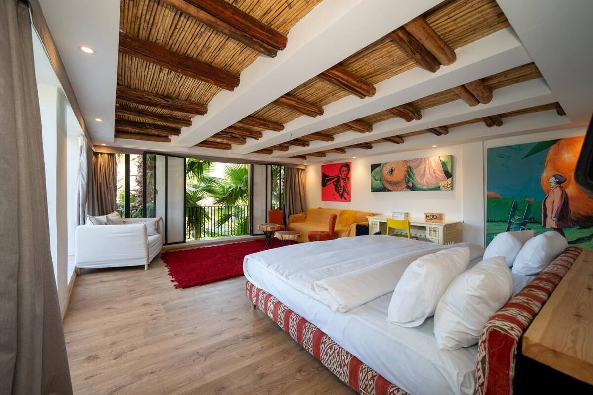 A modern hotel room with a large bed, a sofa, a desk, and a view of the outdoors.