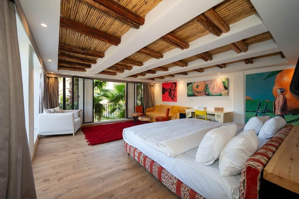 A modern hotel room with a large bed, a sofa, a desk, and a view of the outdoors.
