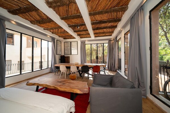 A spacious room with a large window, a wooden ceiling, a dining area, and a sofa.