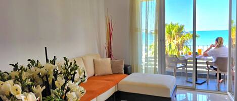A modern hotel room with a large bed, a seating area, a view of the ocean, and a dining area with a table and chairs.