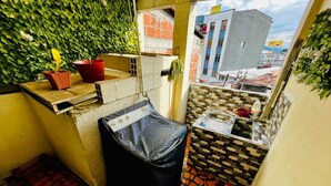 A small balcony with a tiled floor, a black trash bin, a red bucket, and a wall covered in green foliage. - Apartahotel El Progreso (Armenia)