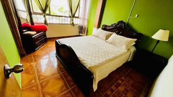 Un dormitorio con cama, cómoda, mesita de noche, lámpara y ventana con cortinas.