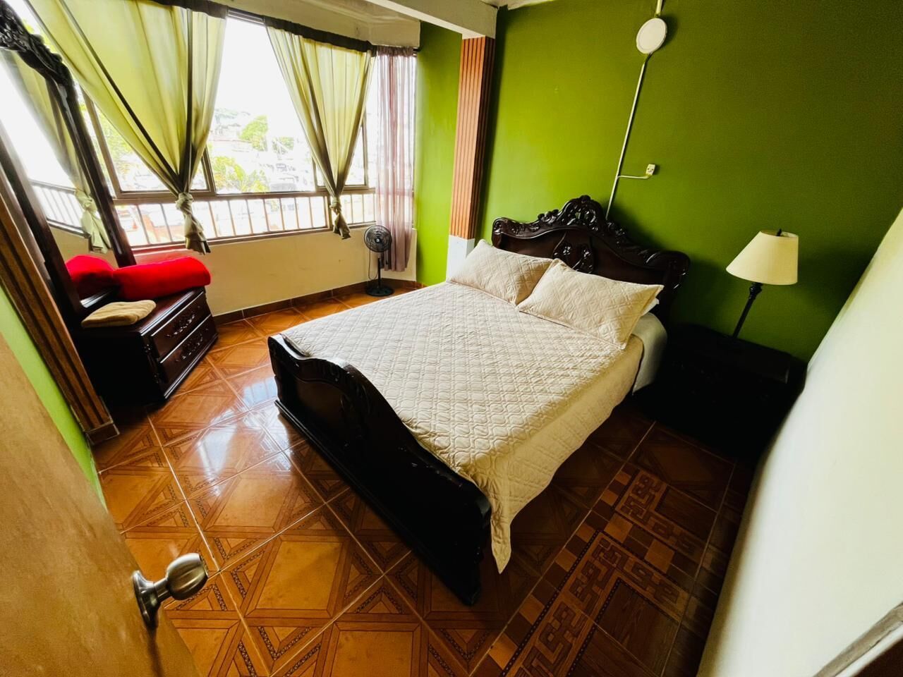 A bedroom with a bed, a nightstand, a lamp, a dresser, and a window with curtains.
