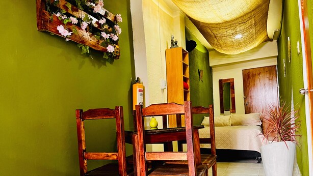 A room with a green wall, wooden furniture, a bed, and a hanging plant. - Apartahotel El Progreso (Armenia)
