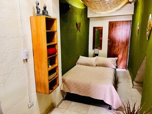 Ein Schlafzimmer mit einem Bett, einem Holzregal mit Dekoration, einem Spiegel und einer grünen Wand.