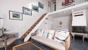A living room with a sofa, a coffee table, a staircase, and a fireplace. - La Proue – Duplex Apartment with Sea View in Arzon, Sleeps 8 (Arzon)